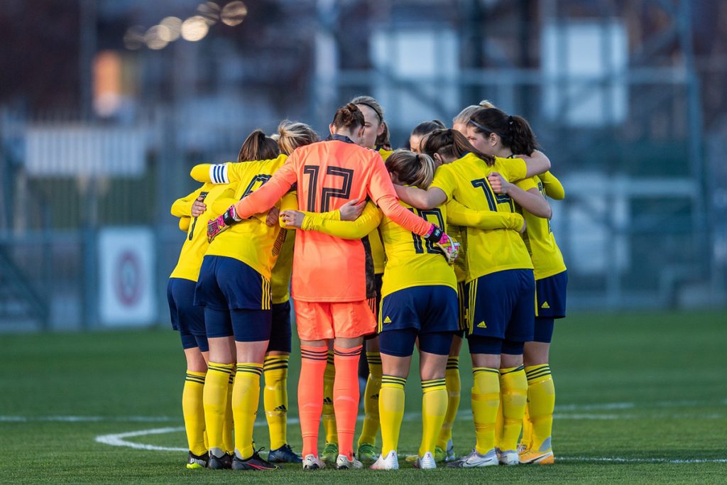 Fotbollsspelare som håller om varandra i en ring mitt p en fotbollsplan.